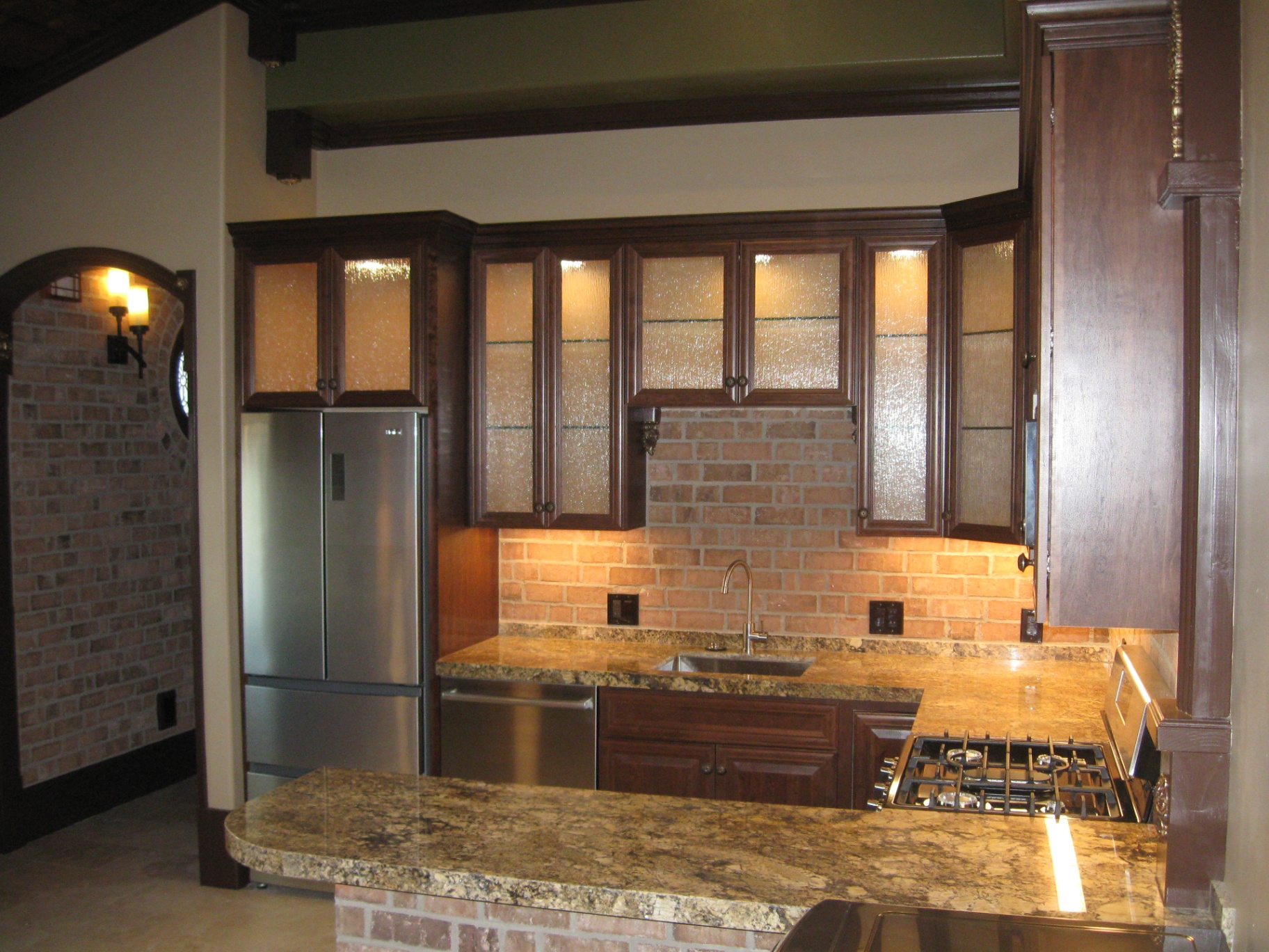 Custom Huntington Beach home kitchen with in-cabinet lighting behind glass panel doors and under-cabinet lighting over brick backsplash