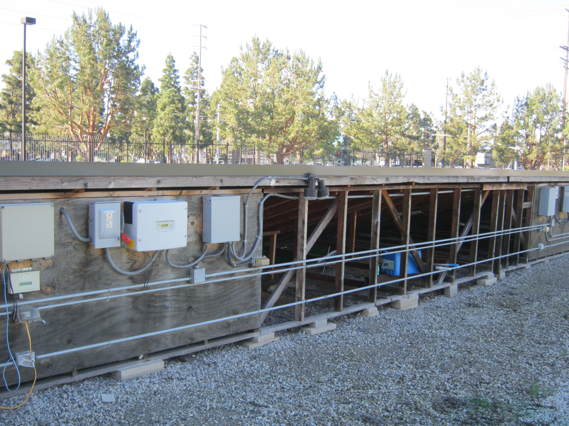 Row of Sharp Solar string inverters, AC disconnects, and rigid conduit runs mounted along a commercial ground-mount PV structure